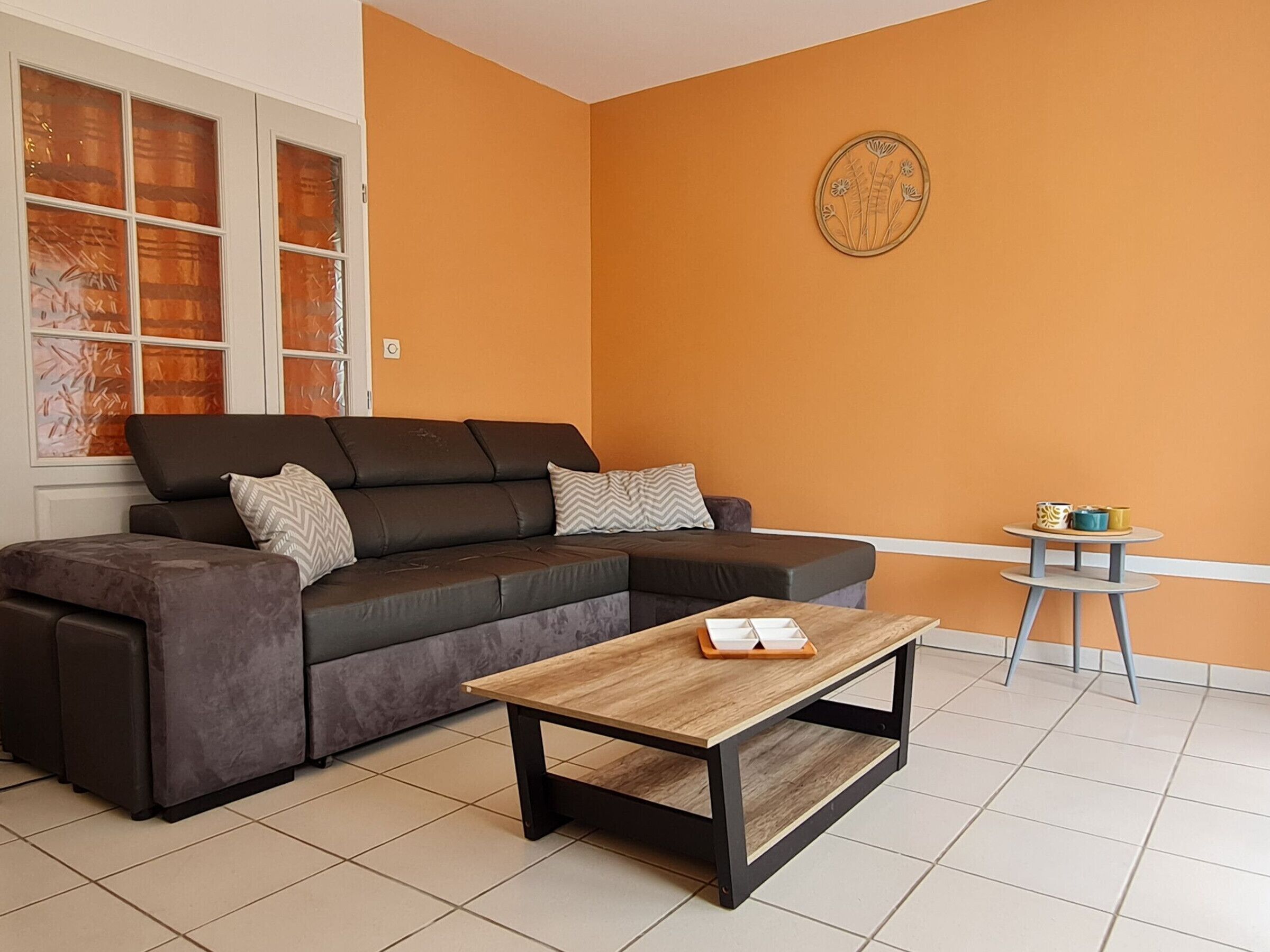 Ein Wohnzimmer mit einem Ecksofa, einem Holztisch, einem kleinen runden Tisch mit Tassen und einer Wanddekoration.