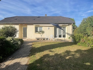 Ein zweistöckiges Haus mit Ziegeldach, einem kleinen Vorgarten und einer Terrasse mit Gartenmöbeln.