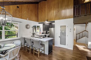 A kitchen with a white island, stainless steel appliances, and a dining area with wicker chairs. - Sequoia Meadow | Fairway Views & BLS Amenities (Arnold)