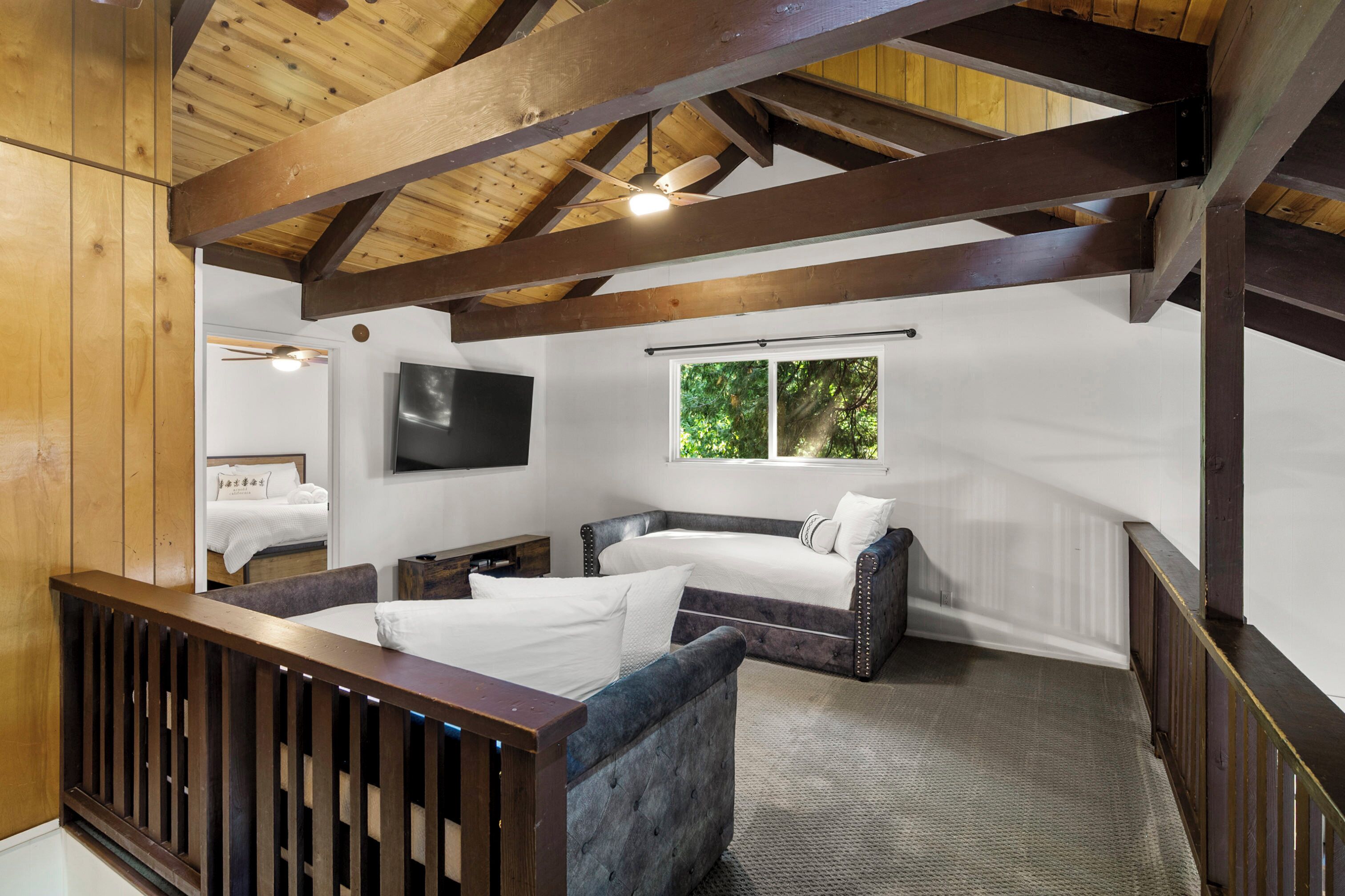 A bedroom with a bed, a sofa, a TV, and a window with a view of trees.
