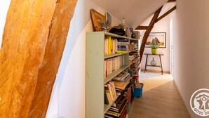A narrow hallway with a wooden beam structure, a bookshelf filled with books, and a small table with a potted plant.