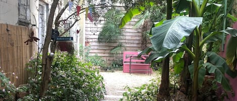 A garden pathway leading to a wooden bench, surrounded by lush greenery and potted plants.