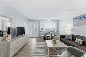 En moderne stue med et fladskærms-tv, en sofa, et sofabord og et spiseområde med stole og et bord.