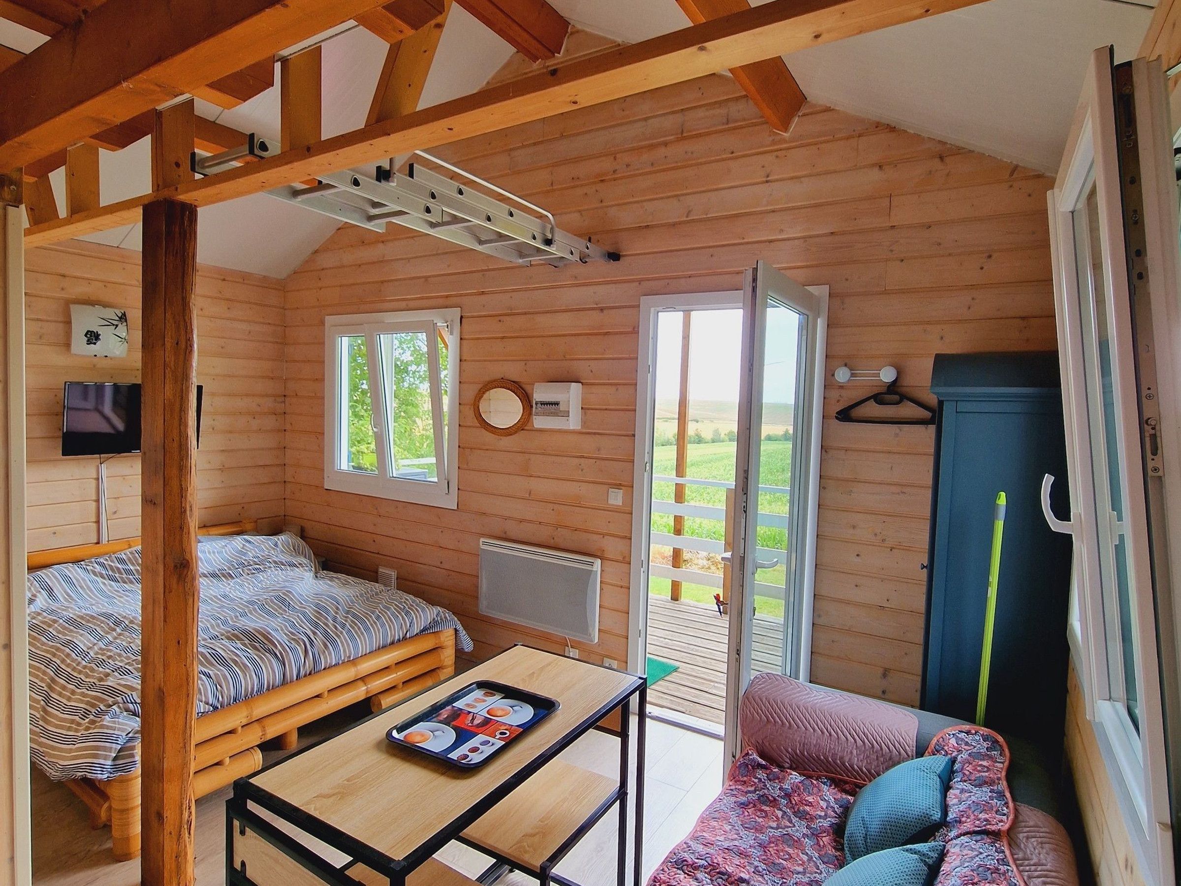 Una cabana de fusta amb un llit, una taula amb una safata, un sofà i una porta que dona a l'exterior.