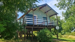 A two-story wooden cabin with a balcony, surrounded by trees and grass.