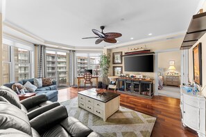 Ein geräumiges Wohnzimmer mit Sofa, Couchtisch, Fernseher und Deckenventilator.