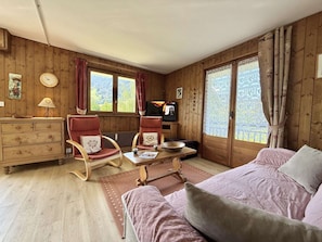 Ein gemütliches Zimmer mit Holzwänden, einem Bett, einem Fernseher, einer Kommode und zwei Stühlen.