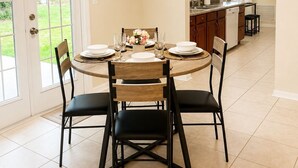 Un comedor con una mesa redonda, cuatro sillas, una araña y vista a la cocina.