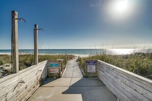 Una passerella in legno che conduce a una spiaggia, con segnali di avvertimento sulle correnti pericolose e assenza di bagnini.