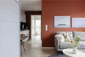 A modern living room with a grey sofa, a coffee table with a vase of flowers, and a painting on the wall. - Orkney - Vacation Rental in St. Peter-Ording, 1 Bedroom (Sankt Peter-Ording)