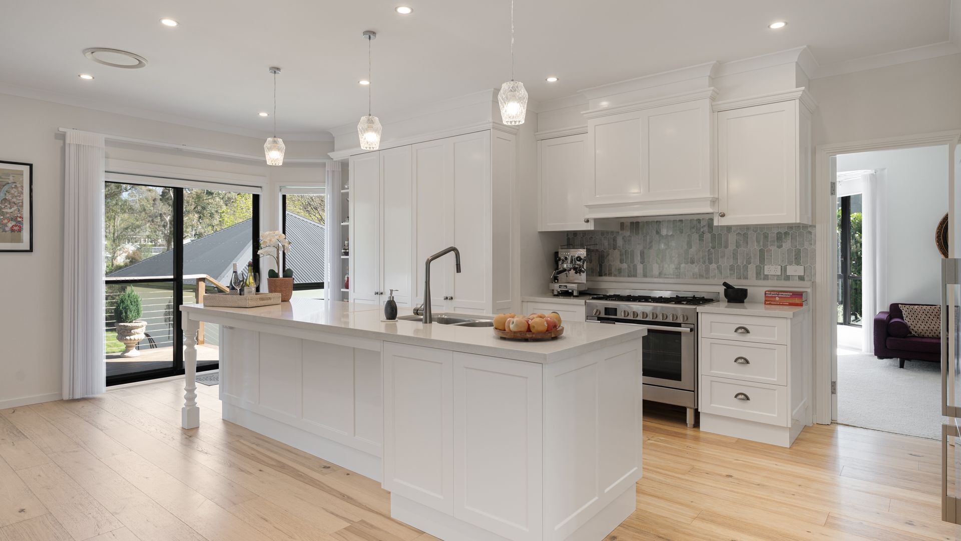 A modern kitchen with white cabinetry, a central island, a built-in oven, and a large window.