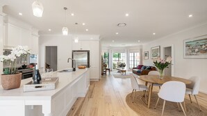 Cozinha moderna com armários brancos, uma ilha central e um espaço de jantar com mesa redonda e cadeiras.