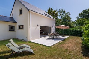 Ein modernes Haus mit überdachter Terrasse, Rasen und Essbereich.