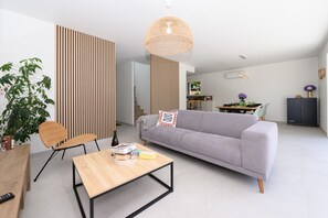 Ein modernes Wohnzimmer mit grauem Sofa, Couchtisch aus Holz und einer Pendelleuchte.