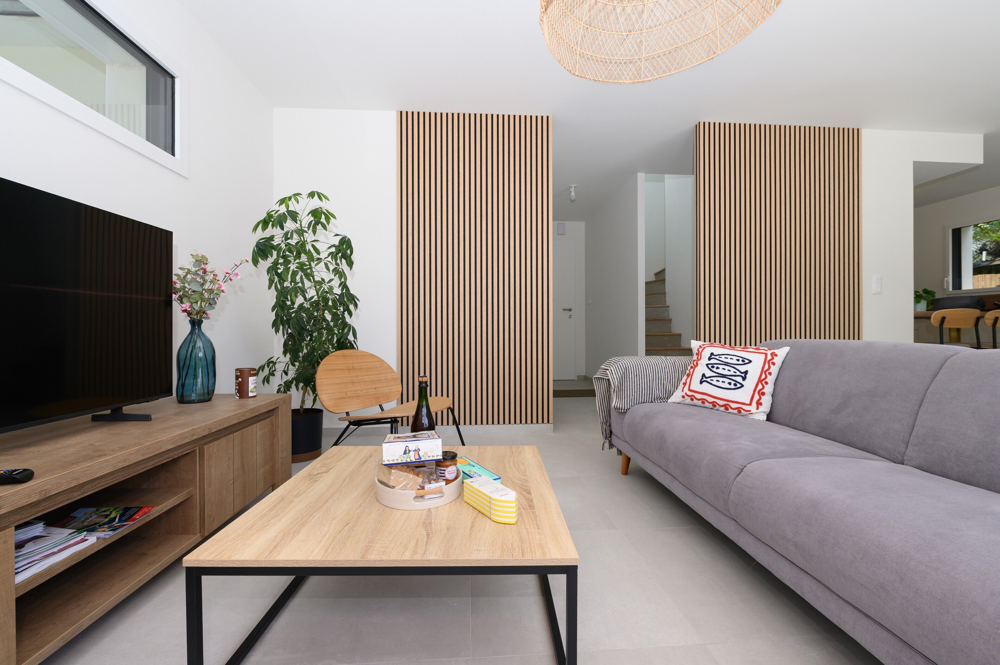 A modern living room with a flat-screen TV, wooden coffee table, grey sofa, and vertical wooden panels.