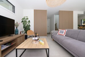 Ein modernes Wohnzimmer mit Flachbildfernseher, Holztisch, grauem Sofa und vertikalen Holzpaneelen.
