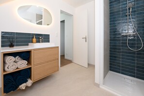 Une salle de bain avec une douche, un miroir et une étagère où sont rangées les serviettes.