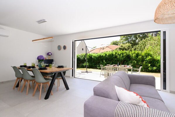 Ein modernes Interieur mit Essbereich, einer Couch und einer großen Schiebeglastür, die auf eine Außenpatio führt.