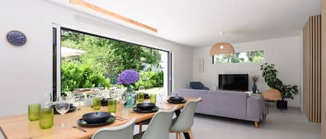 Una sala de estar moderna con sofá, televisor y comedor con sillas y una mesa.