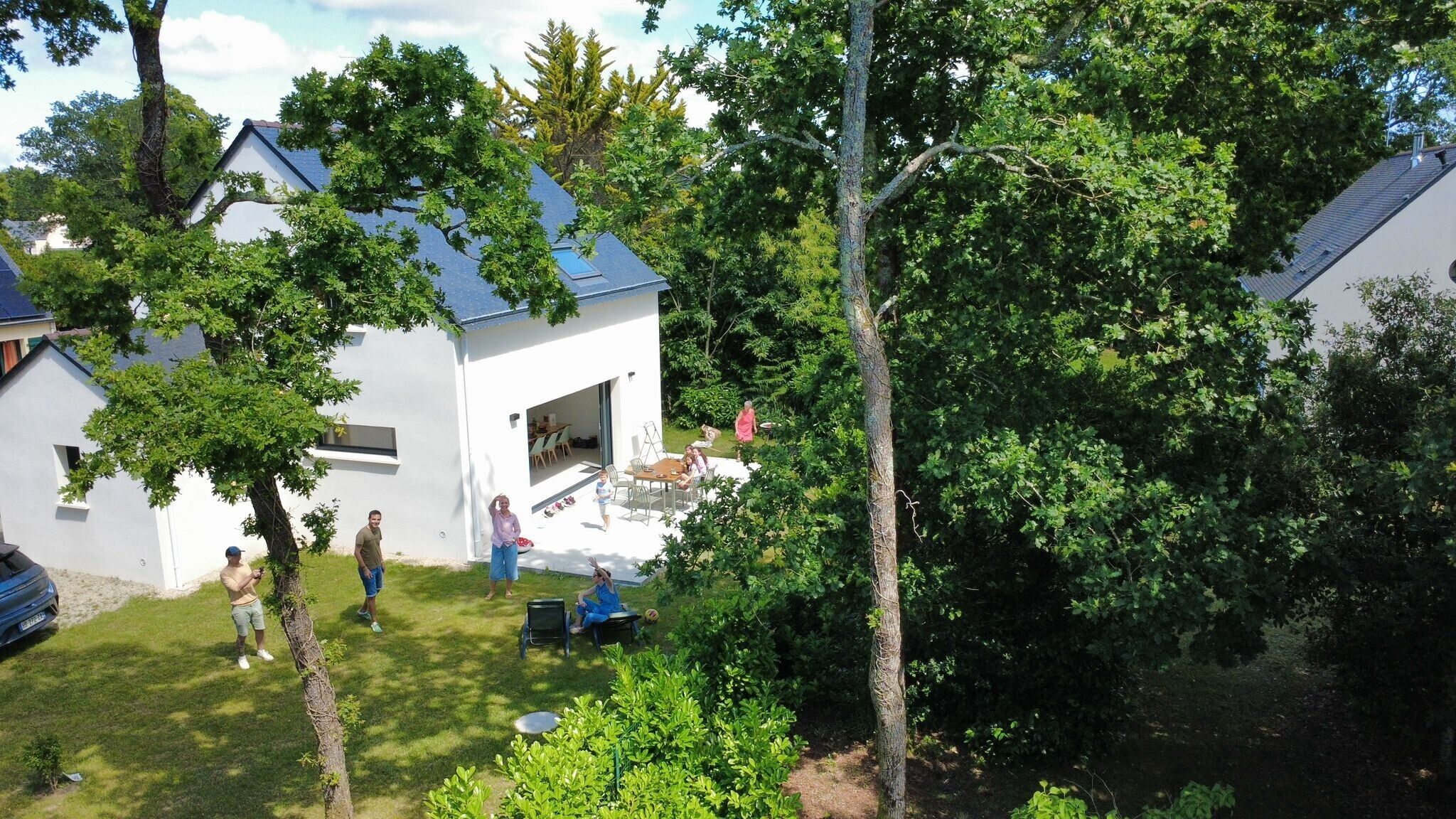 A modern house with a white exterior, a visible patio area, and a large tree in the foreground.