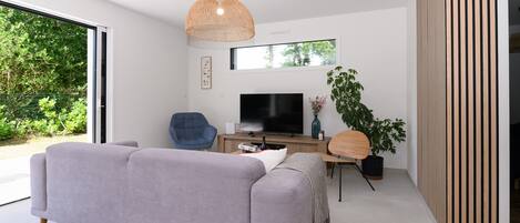 Una sala de estar moderna con un sofá gris, un televisor, una lámpara colgante de mimbre, un aparador de madera y un ventanal grande.