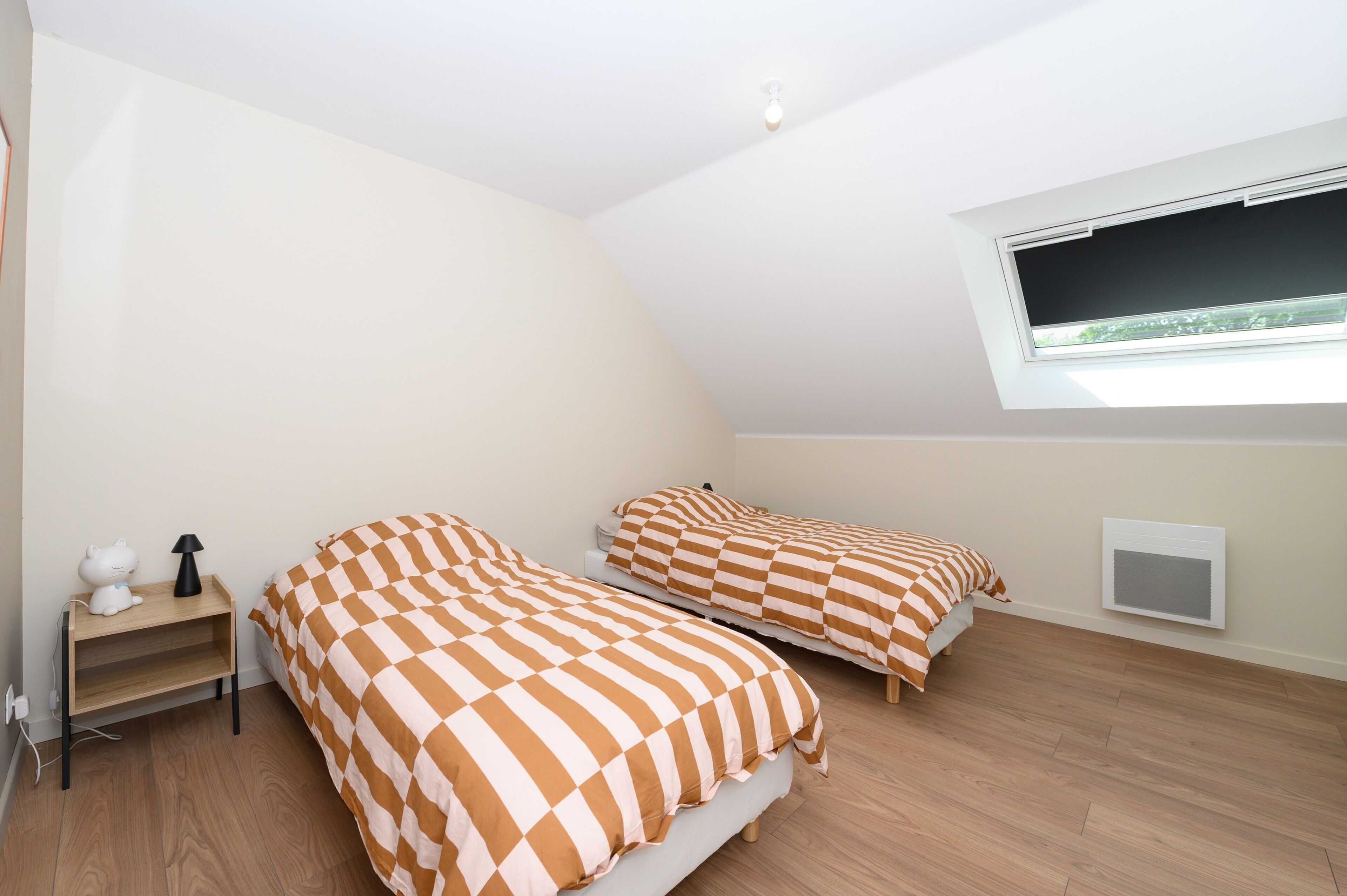 Een slaapkamer met twee bedden, een nachtkastje, een lamp en een raam met uitzicht.