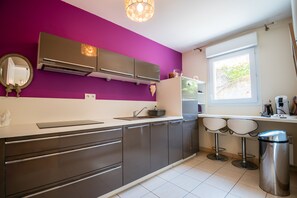 Una cocina moderna con pared morada, electrodomésticos de acero inoxidable, una ventana y dos taburetes de bar.