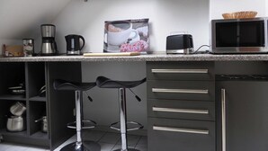 Une cuisine moderne équipée d’un plan de travail, d’une machine à café, d’un four à micro-ondes et d’un tabouret de bar.