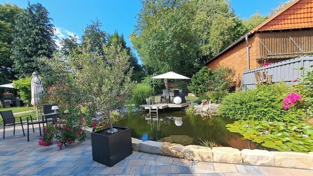 Un jardin avec un étang, un espace aménagé pour s’asseoir à l’extérieur et un bâtiment en briques.