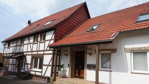 Il s’agit d’un bâtiment traditionnel à colombages, doté d’un toit recouvert de tuiles rouges, d’une entrée principale avec des marches et d’un petit porche.