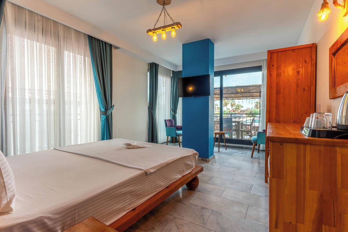 A hotel room with a bed, a TV, a wooden desk, and a balcony with chairs.