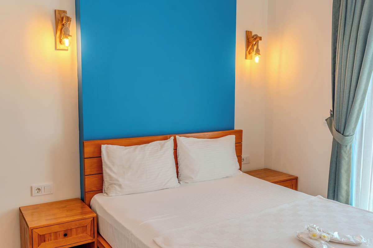 A hotel room with a wooden bed, white bedding, two bedside tables, and wall-mounted lights.