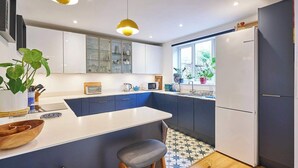 Una cocina moderna con una isla central, taburetes de bar, un refrigerador y una ventana con plantas.