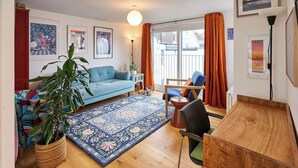 Una sala de estar con un sofá, una mesa de comedor, una silla, una planta grande y una alfombra.