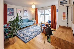 A living room with a sofa, a dining table, a chair, a large plant, and a rug.