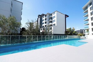Ein modernes Gebäude mit Schwimmbad, Balkonen und blauem Himmel.