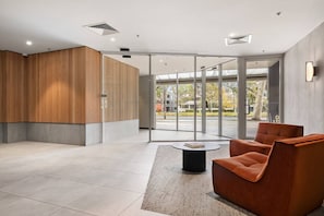 A modern lobby with a wooden accent wall, a glass door leading outside, and a seating area with a round table. - Heart of city/modern 2BR/free parking/ANU/pool/gym (Braddon)