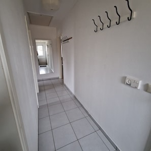 Un pasillo estrecho con suelo de baldosas blancas, un perchero y un termostato fijado a la pared.