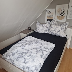 Un letto con una coperta a motivi bianchi e grigi, un comodino in legno con una lampada e due opere d'arte appese al muro.