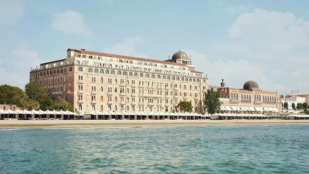 Ein großes, historisches Gebäude mit mehreren Stockwerken und einer Kuppel, in Strandnähe mit Liegestühlen.
