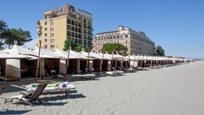 Ein Strand mit Liegestühlen und Sonnenschirmen, ein Hotelgebäude und ein klarer Himmel.