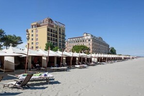 A beach with rows of sunbeds and umbrellas, a hotel building, and a clear sky. - Elegant Family Apartment with Terrace & Shared Garden, Steps from Lido Beach (Lido)