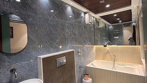 Uma casa de banho moderna com parede de mármore, banheira, sanita e lavatório.