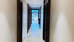 Um corredor com chão de mármore, portas de madeira escura e vista para uma área de estacionamento.