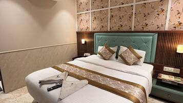 A hotel room with a large bed, a ceiling fan, an air conditioning unit, a nightstand, and a wall with floral wallpaper.