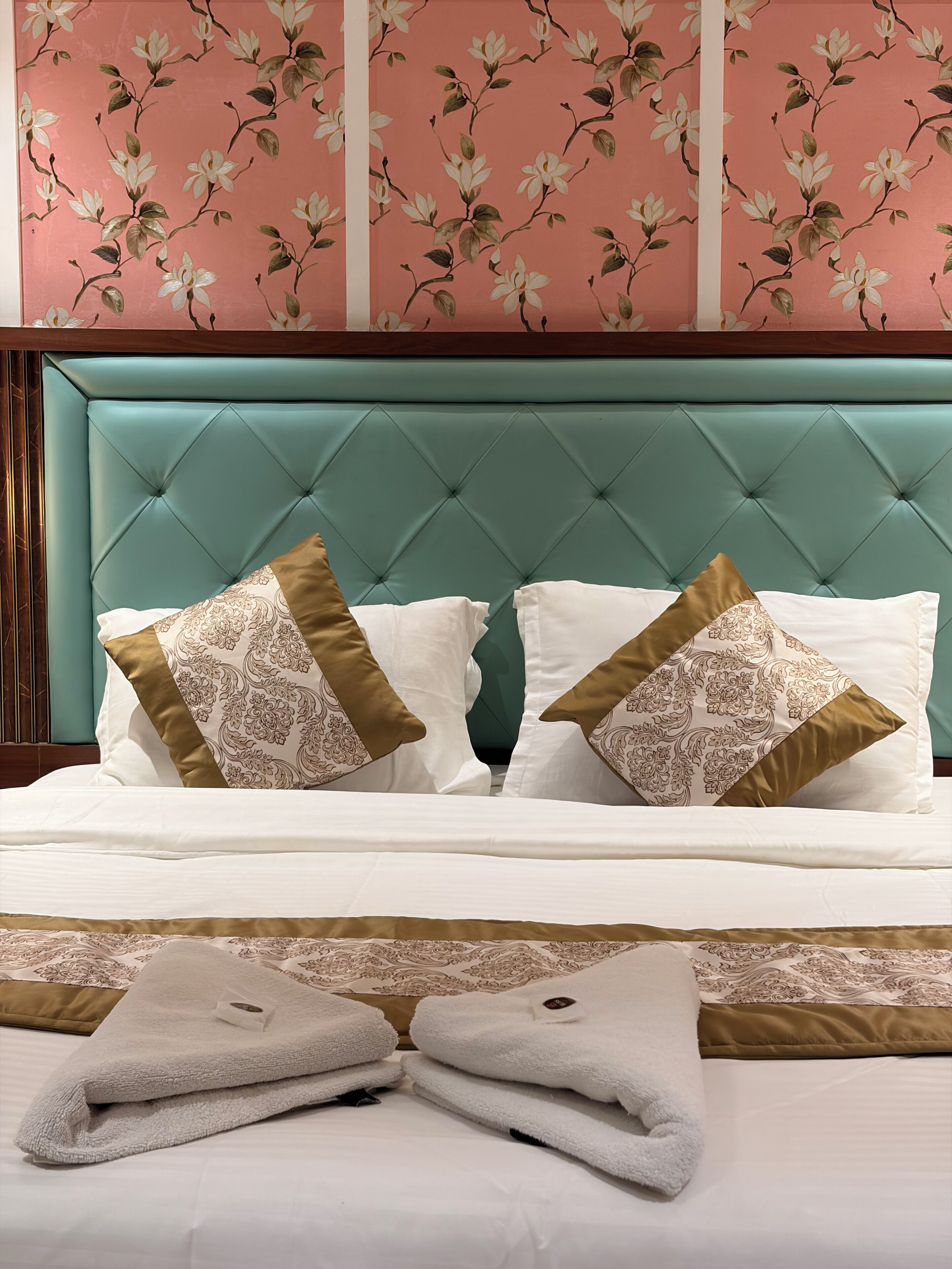Una cama con cabecera capitonada, dos almohadas decorativas y toallas dobladas.
