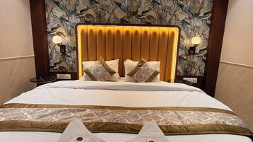 A hotel room with a large bed, a headboard with a floral pattern, and a bedside table with a lamp.
