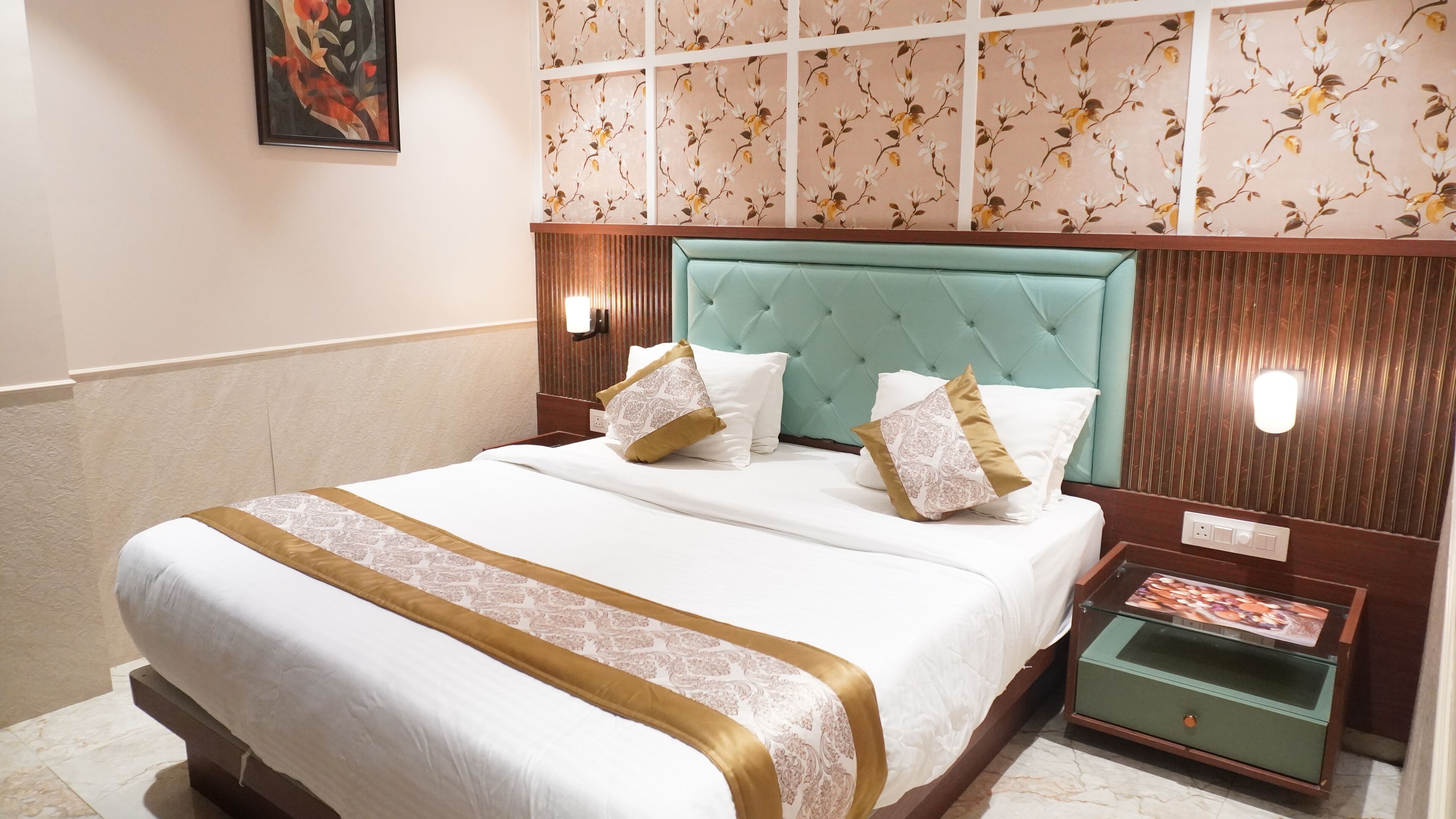 A hotel room with a bed, a nightstand, a wall-mounted lamp, and a floral-patterned wallpaper.