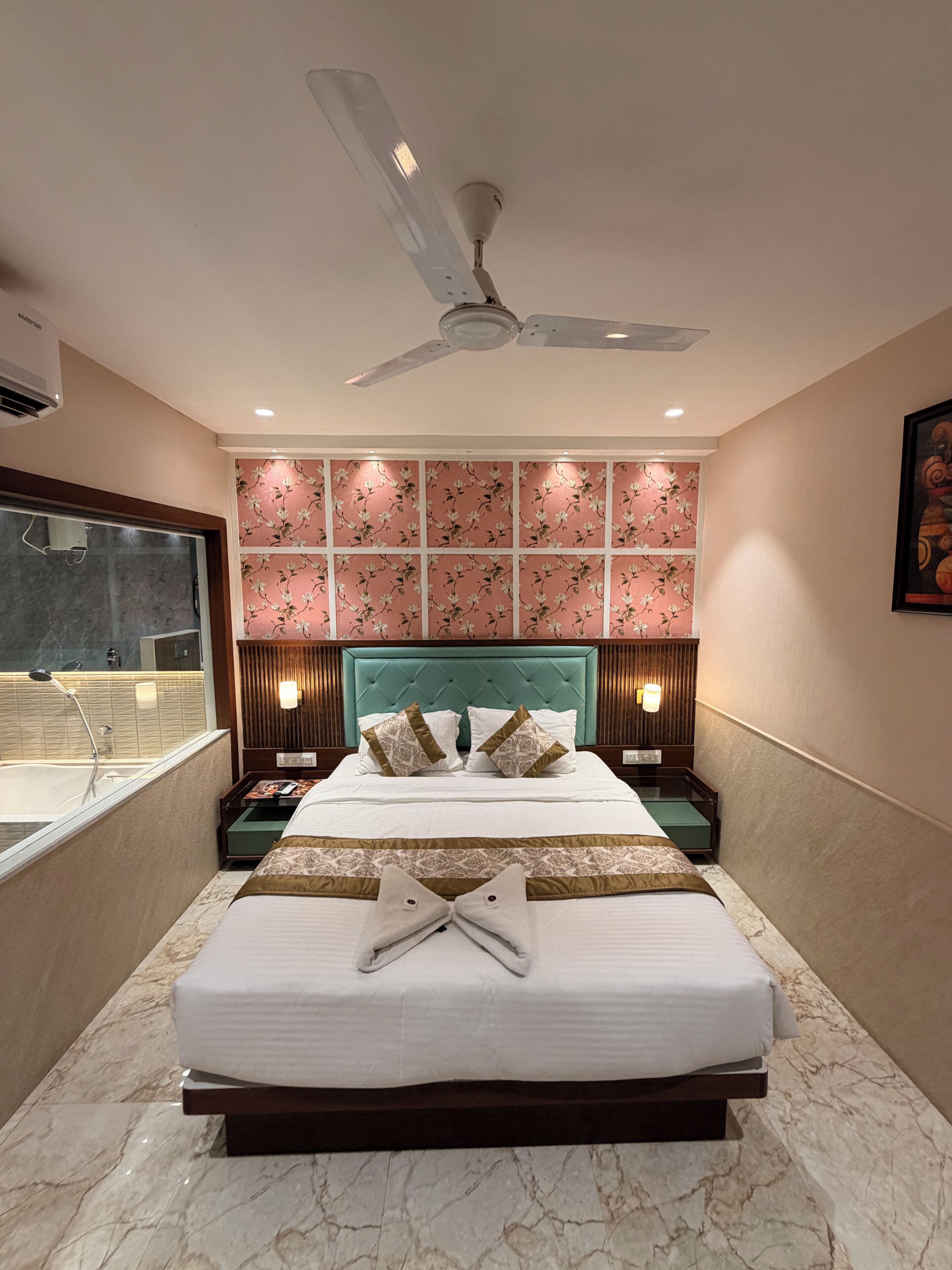 Una habitación de hotel con una cama grande, un ventilador de techo, un baño con bañera y un panel decorativo en la pared.