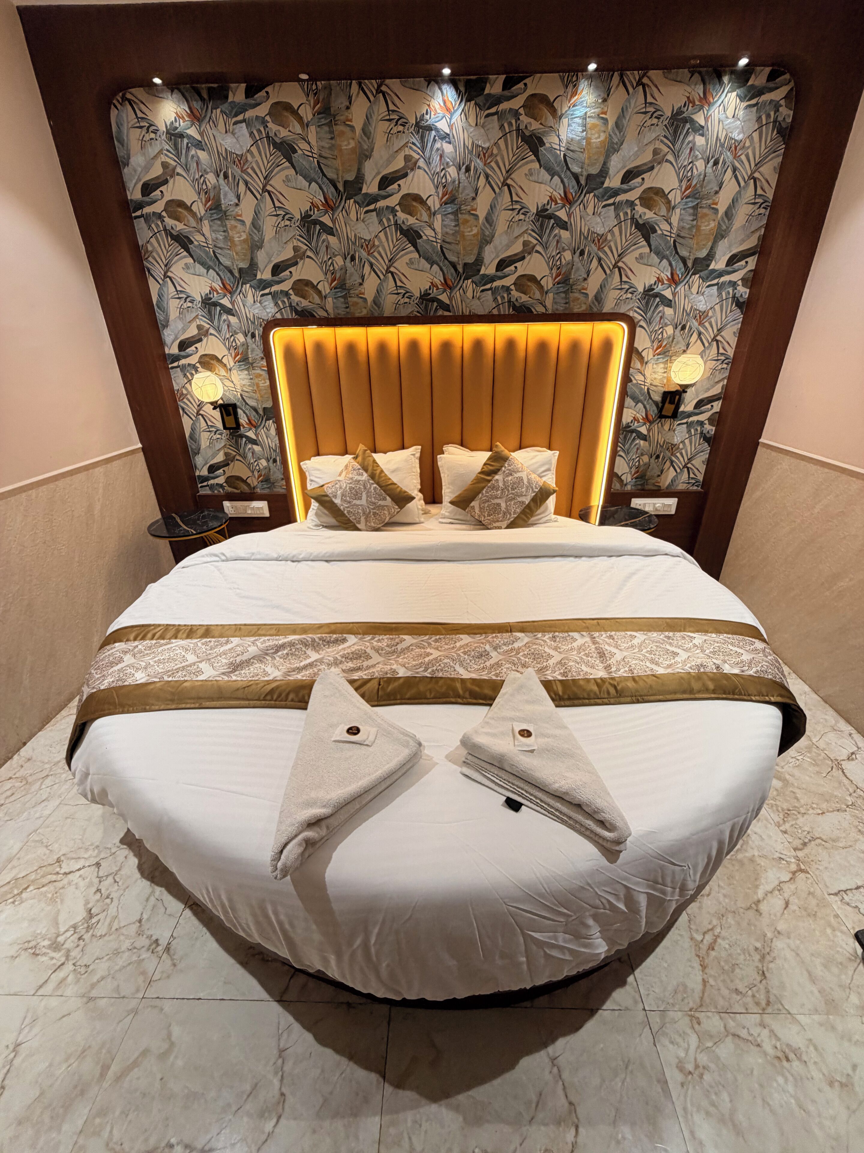 Una habitación de hotel con una cama grande, cabecera con estampado floral y lámparas de noche.